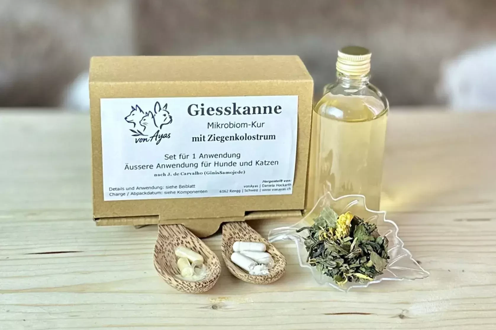 Die Giesskanne Mikrobiom-Kur mit Ziegenkolostrum, Kombucha, Kapseln und Kräutermischung auf einem Holztisch.
